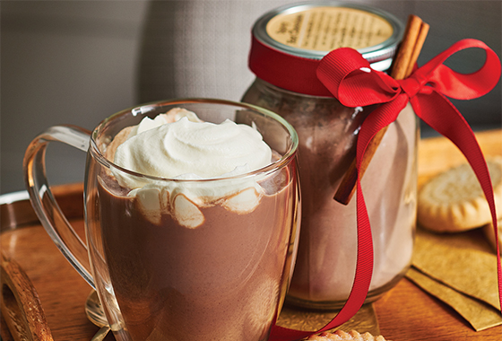 Clear mug of hot chocolate with whipped cream on top.