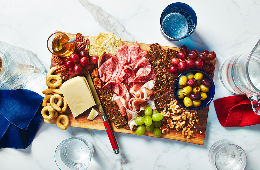 Salami, crackers, cheese, olives, and grapes on wooden board.