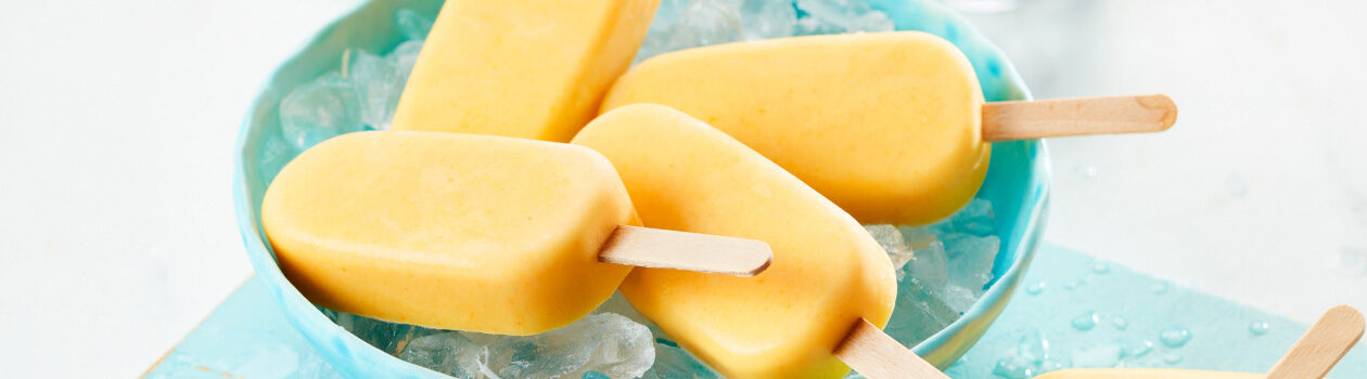 Several golden milk smoothie pops in a light blue bowl sitting a top ice.