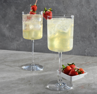 A gin-based drink in an ice-filled goblet starring Betty Buzz Sparkling Lemon Lime and fresh basil. Garnished with strawberries on a pick.