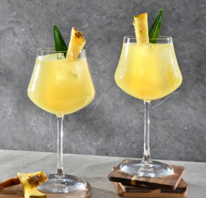 Betty Buzz Ginger Beer, pineapple juice and gin in a curvy sling glass topped with pineapple spear, placed on coasters next to each other.