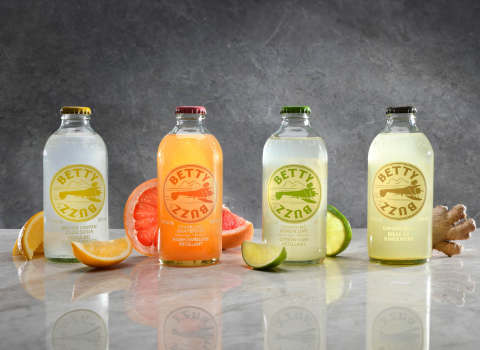 4 bottles of Betty Buzz flavoured drinks with corresponding fruits presented on a marble countertop.