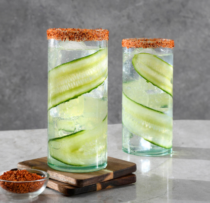 Two glasses rimmed with spice featuring Betty Buzz Meyer Lemon Club Soda and tequila lined with cucumber ribbon and place next to each other.