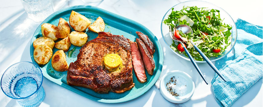 blue serving plate with large grilled rib steak with compound butter on top