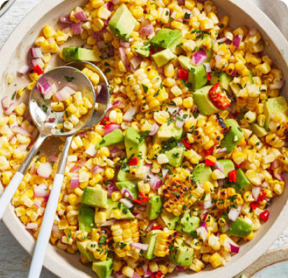 Corn and avocado salad in large bowl with serving spoon
