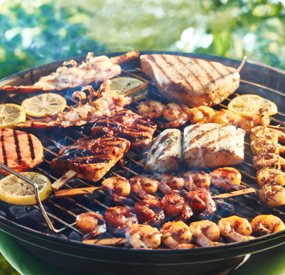 Round bbq grill top with cooked fish fillets, shrimp skewers, tuna steaks, lemon slices