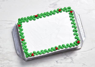 marble surface with rectangular white slab cake on silver sheet, with green and red holly buttercream edging and no centre decoration