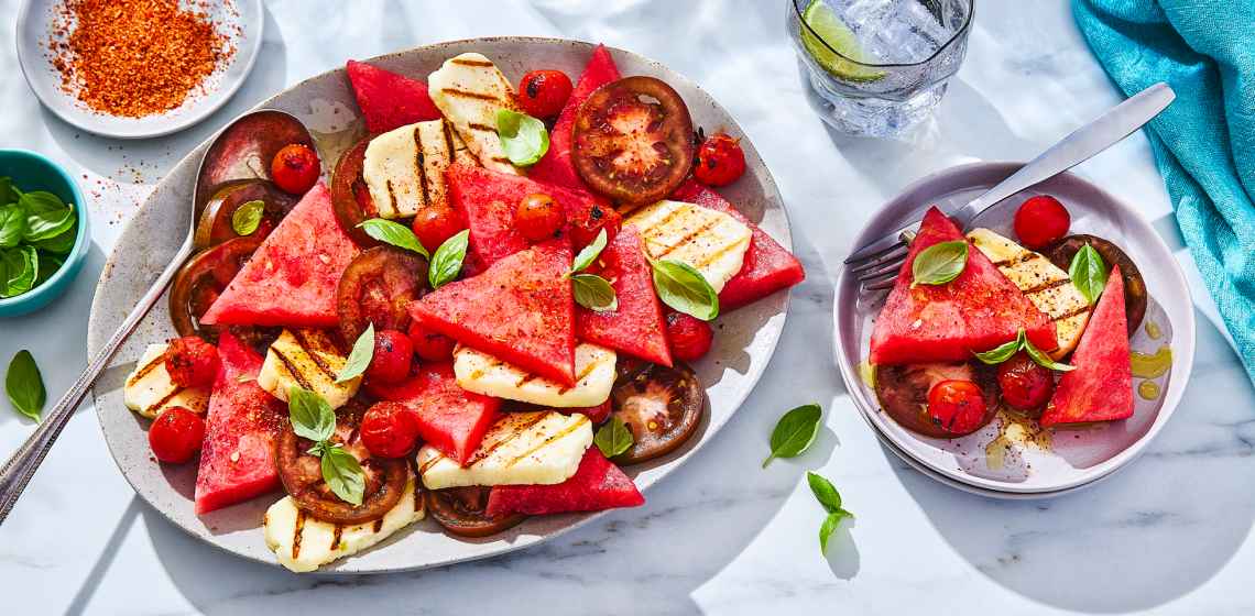 large white platter of grilled halloumi and watermelon salad, with small side plate of salad served out to the right side.
