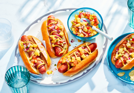 blue platter of three loaded hot dogs with one side plate of a hot dog and chips to the side